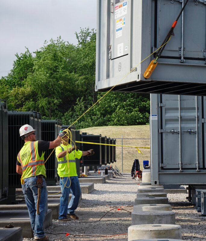 Two workers with rope guide containerised BESS units into place at the McHenry battery project in Illinois, which EDF bought from developer Glidepath.